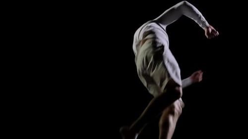 Athletic Man in White Clothes Performs Tricks Jumping on a Trampoline on a Black Monophonic
