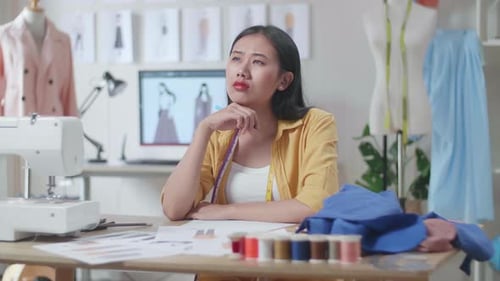Asian Female Designer With Sewing Machine Thinking While Designing Clothes In The Studio
