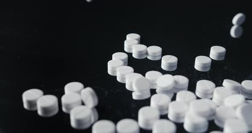 White Pills Falling onto a Dark Surface