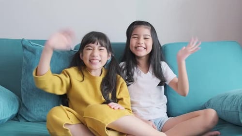 Cheerful Girls Waving From Blue Couch at Home