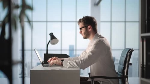 Portrait of Thoughtful Successful Businessman Working on Laptop Computer in His Big City Office