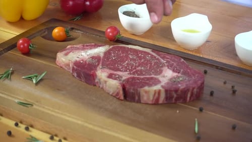 Chef cook season fresh chunk of deli piece of beef with sea salt and grounded spicy peppers.