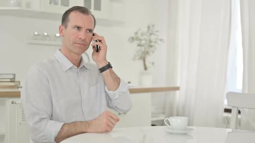 Man Sitting at Table Talking on Smartphone