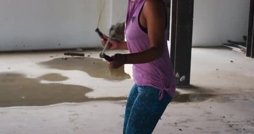 African american woman wearing hoodie skipping rope in an empty urban building