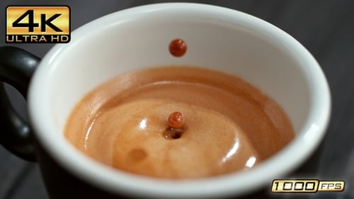 Ralenti macroscopique : une goutte de café tombe dans la tasse à expresso et une crème mousseuse fait sensation