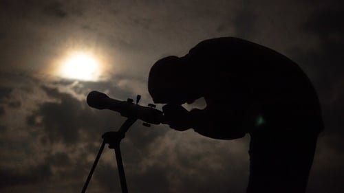 Человек смотрит в телескоп на ночное небо под луной