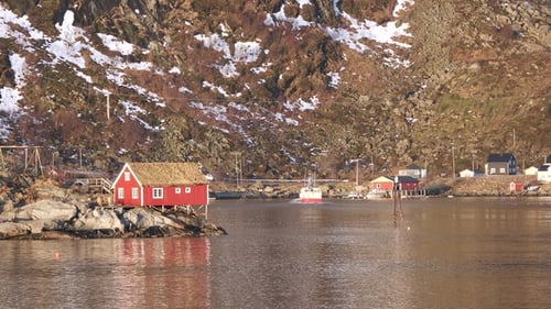 Traditional red cabins stand by the tranquil waters surrounded by snow-capped mountains. Lofoten.