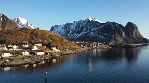 Scenic view of a coastal village in Norway surrounded by mountains at sunset.