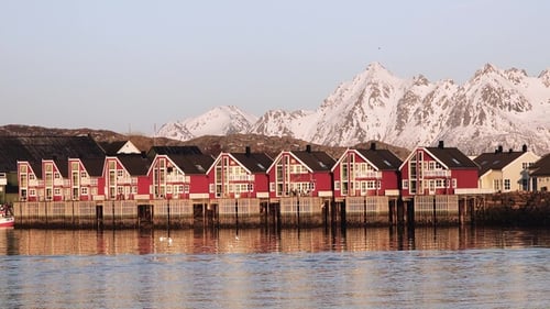 Beautiful red houses on a dock with snow-capped mountains in the background during daytime