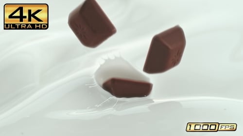 Chocolate chunks falling into white cream in slow motion