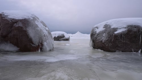 Snenic icy seashore with a boulders covered in ice and snow.