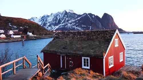 Red cabin by the water with mountains in the background during golden hour in Norway