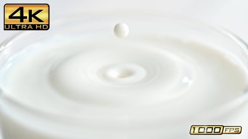 Ein Glas Milch auf einem hellen Küchentisch und tropfendes Tröpfchen, das in Zeitlupe für Spritzer sorgt