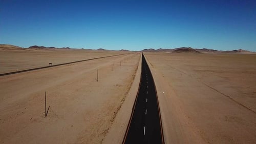 Long road stretches through desert landscape under clear blue sky in remote location during daytime