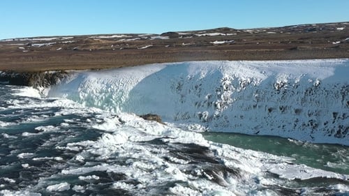 Majestätischer Wasserfall, der über felsige Klippen in einer Winterlandschaft kaskadiert.