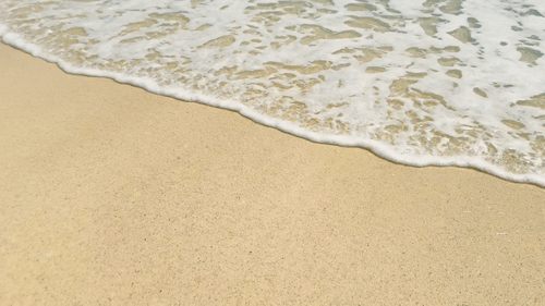 Clean foaming sea waves splashing on a white sand beach on a sunny summer day. Calm water waves.
