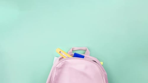 Colorful school supplies moving from school pink bag on mint green background.