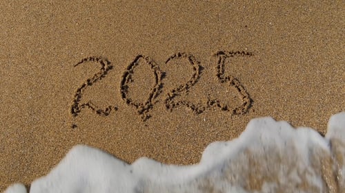 A number written in the sand representing the year 2025 disappears with the help of a sea wave.