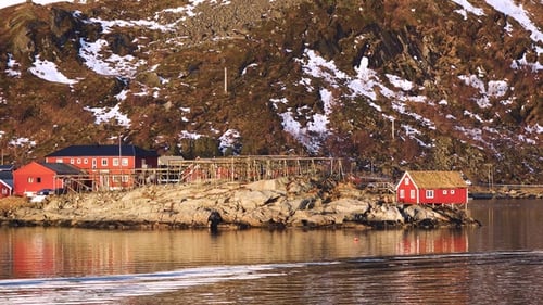 Red cabin by the water with mountains in the background during golden hour in Norway