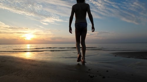 Young Adult Walking on Beach at Sunset