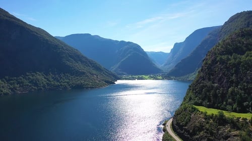 View of river and road in Norway with mountains in the background and cars driving on a sunny day