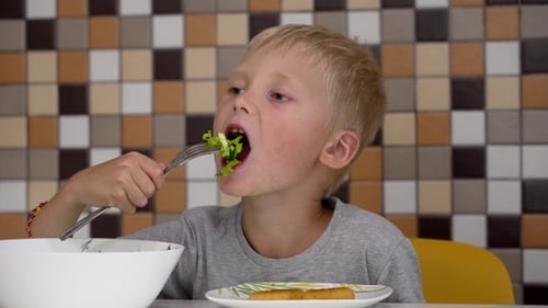Child Eats Green Salad at the Table
