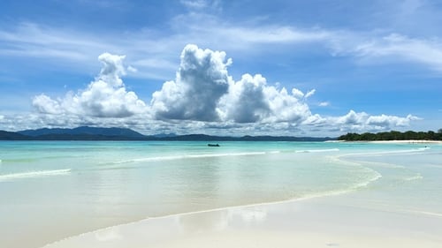 Strandblick mit Wolken, Boot und Bergen im Hintergrund an sonnigen Tagen