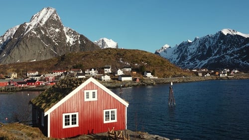 Cottage on the shore of the fjord. Beautiful mountains covered white snow. Lofoten Island, Norway.