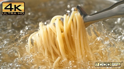 Lifting Cooked Pasta from a Pot of Boiling Water Using Spaghetti Tongs and Splashing Water Droplets