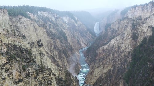 Yellowstone. Snow falls gently on a spectacular waterfall cascading amidst tall evergreen trees.