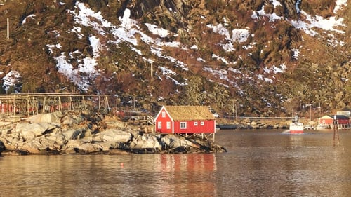 Exploring a traditional red cabin by the water with stunning mountain backdrop in Norwa