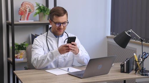 Male doctor medical worker in modern clinic wearing eyeglasses and white coat uniform using phone