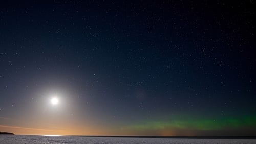 Timelapse. Sea covered with ice under a starry sky with moon and northern lights.