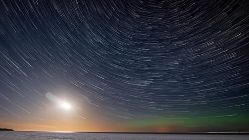 Timelapse. Star trails, moon trail and northern lights above the sea covered with ice.