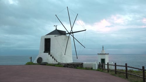 Windmill by the ocean. Historic traditional Azores windmill. Blue sky and clouds behind windmill.