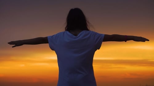 Silhouette of a girl with her arms raised to the sides against the backdrop of a beautiful sunset