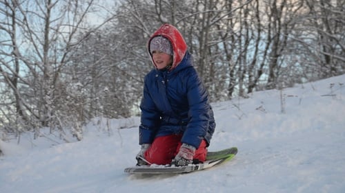 Happy child rides a sled down a snowy slope. Slow motion