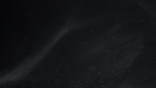 Turbulence dust particles rise into the air on a black background in slow motion