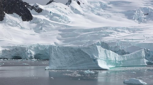 Large iceberg floats in clear waters under a bright blue sky, showcasing the beauty of Arctic nature