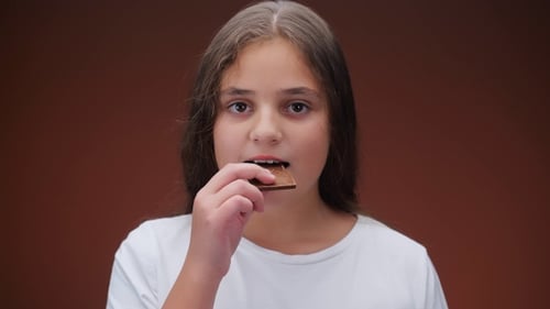 Caucasian Girl Eating Chocolate Bar on Brown Background