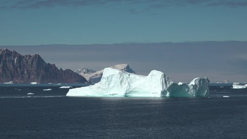 Iceberg floating in ocean under clear sky, showing large structure and blue tones in environment