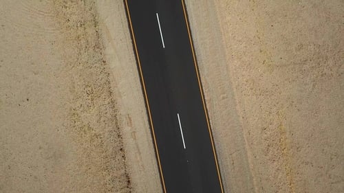 Long road stretches through desert landscape under clear blue sky in remote location during daytime