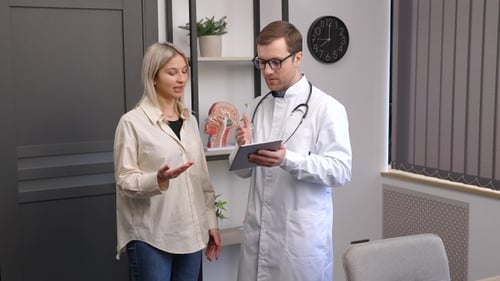 Happy man doctor showing tablet woman patient in clinic office interior. Health care