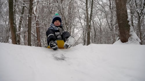 Die Brüder rutschen abwechselnd eine Eisrutsche in einem Winterwald hinunter.