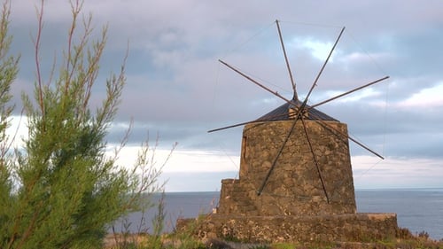 Windmill by the ocean. Historic traditional Azores windmill. Blue sky and clouds behind windmill.