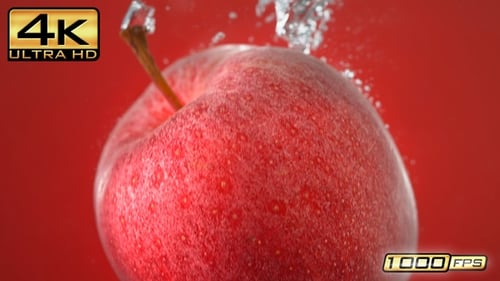 Une pomme tombée dans l'eau fait des bulles et coule vers le bas sur fond rouge, Ralentissement, macro
