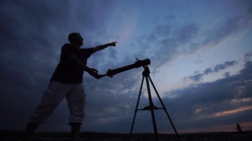 Man looks through a telescope at the evening sky