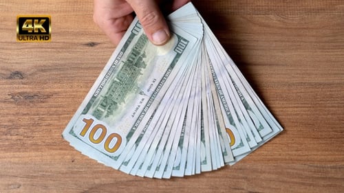 Hand Places One Hundred Dollar Bills on Wood