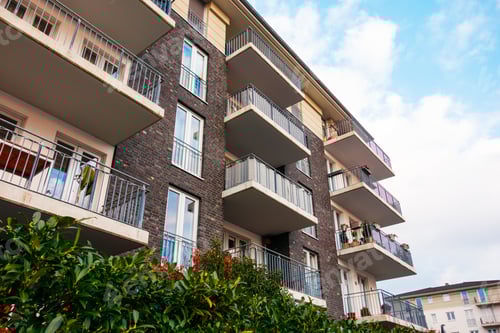 Preview: Brown And Brick Facaded Apartment Building With Green Bush In The Foreground