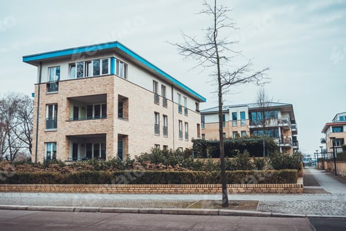 Preview: Modern Brick Apartments With Blue Rimmed Roof And Bare Tree Near Sidewalk In Front